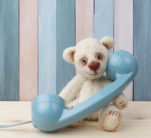 A vintage toy teddy bear with a telephone on old wooden wall background