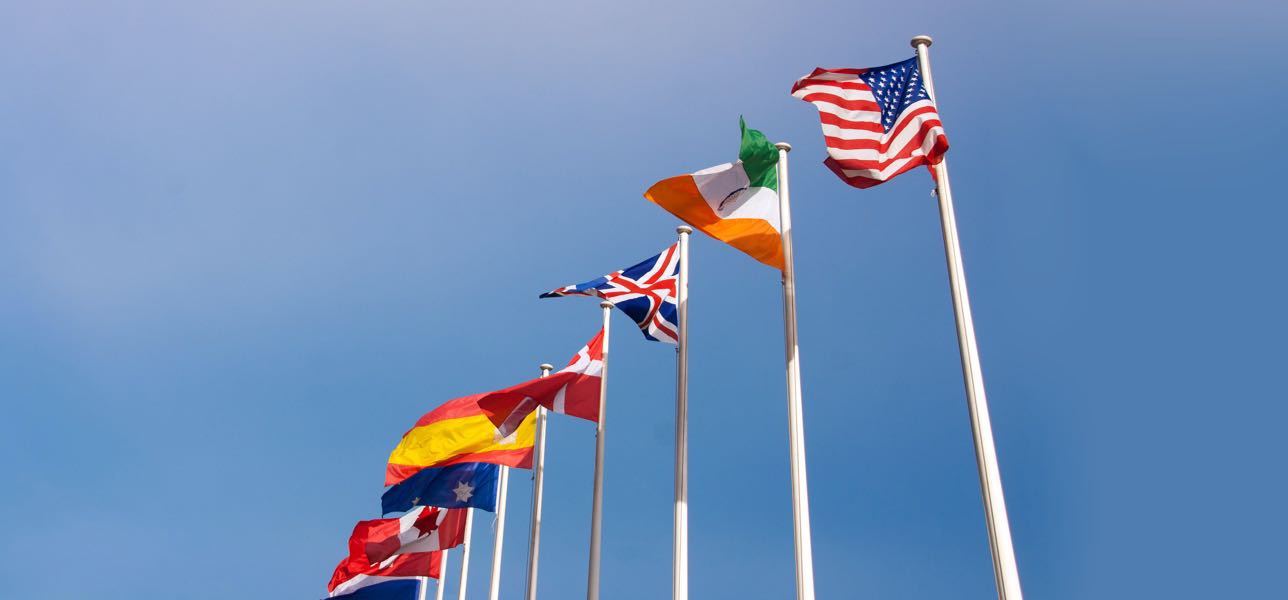 International countries flags on white flag poles against a bright blue sky
