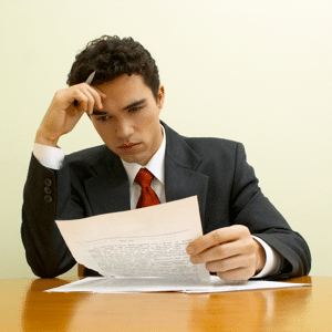 A young businessman is sitting at a polished table attentively reading a document