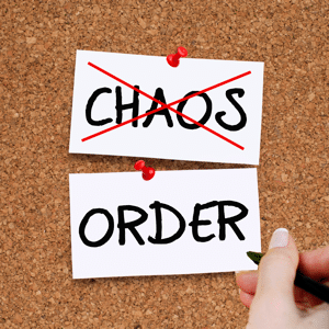 CHAOS crossed out in red and a woman writing ORDER on a cork noticeboard