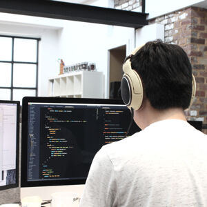 A view from behind of an IT developer wearing headphones coding at a computer