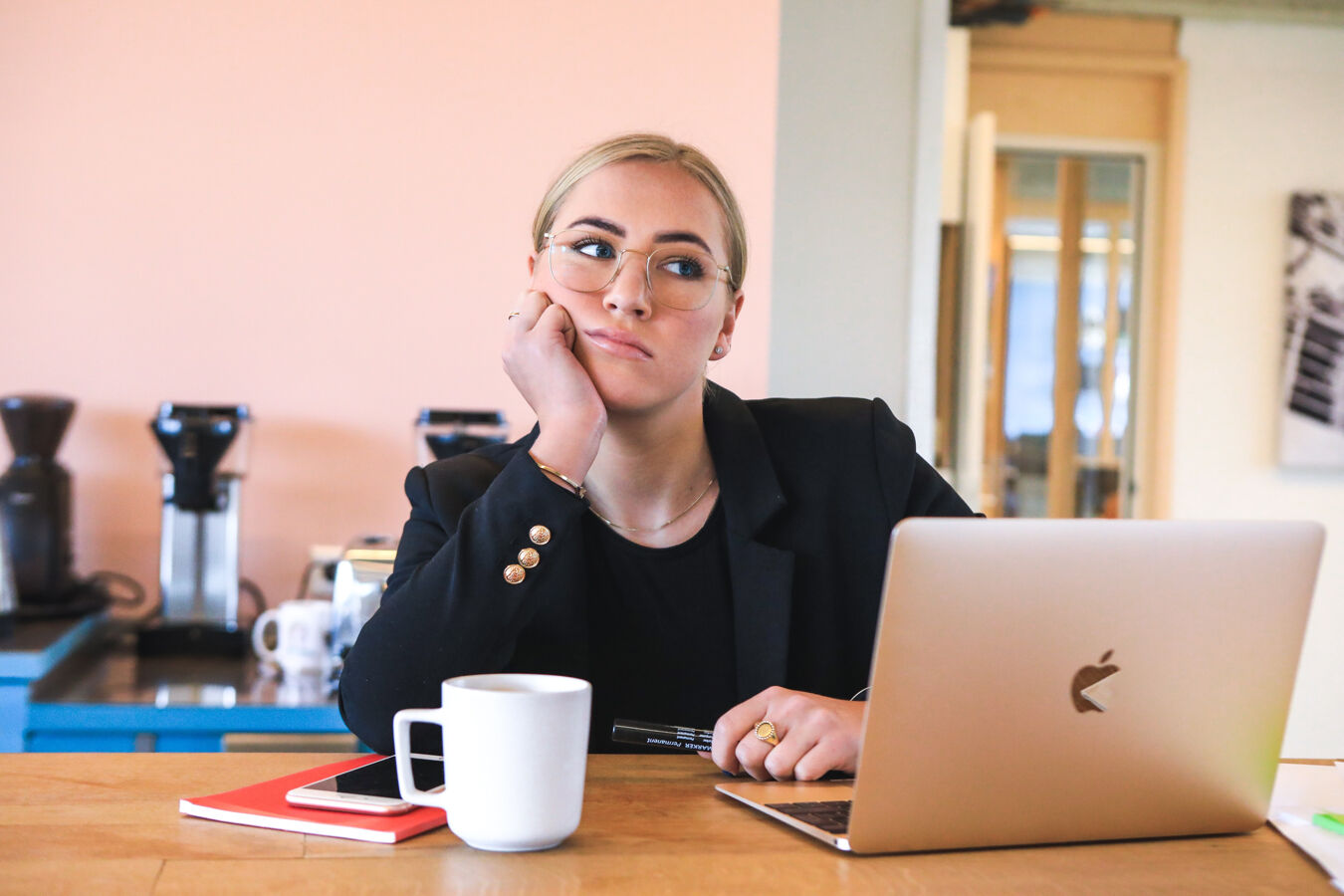 A business woman in an office setting looking fed up behind a silver Apple laptop computer