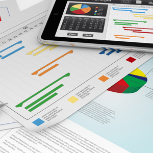 A tablet computer displaying a Gantt chart along with a selection of colourful business charts displayed on a desk