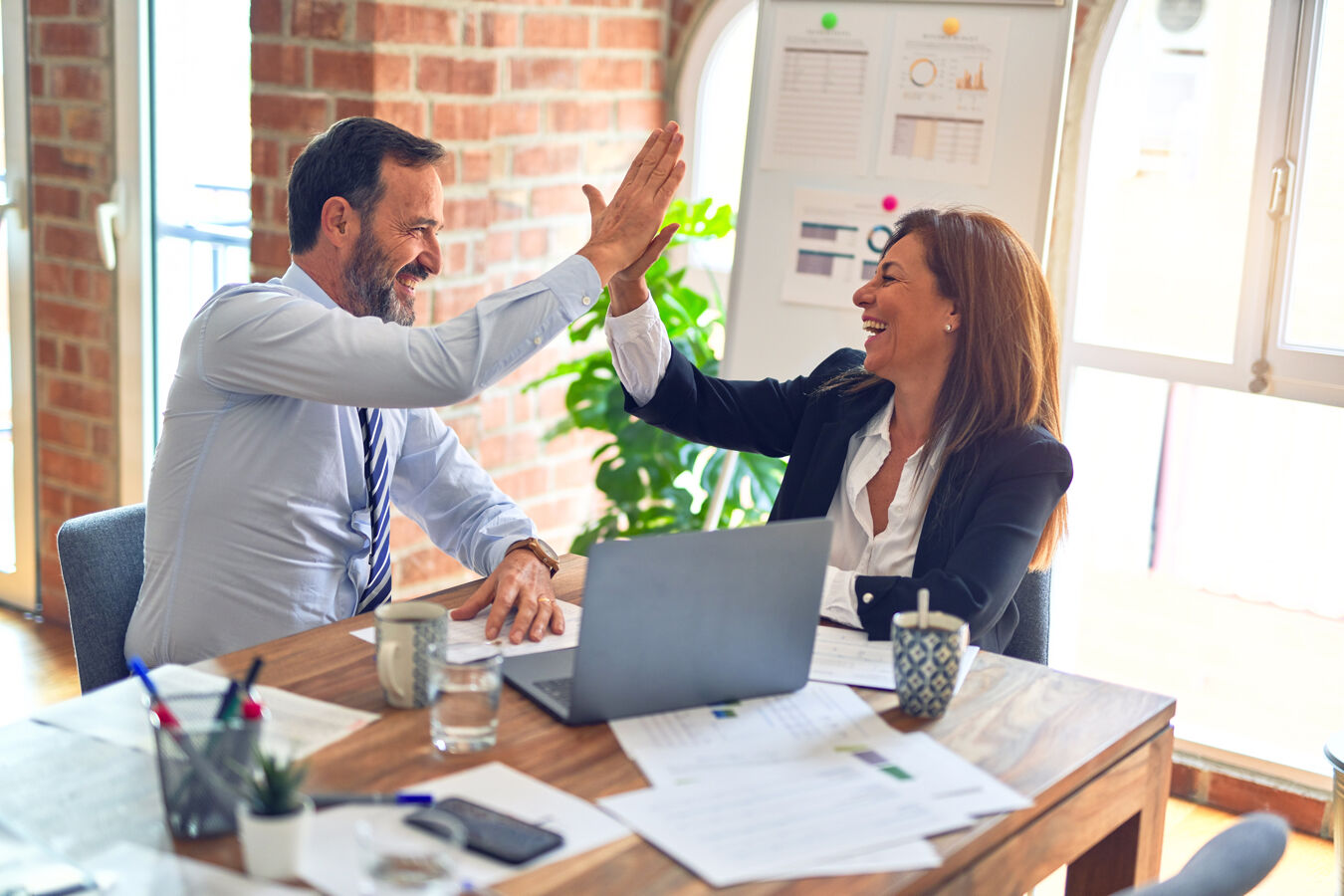 A smart businessman and businesswoman high-fiving in a modern office setting