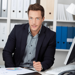 Smart young project manager with graphs sitting by computer at an office desk