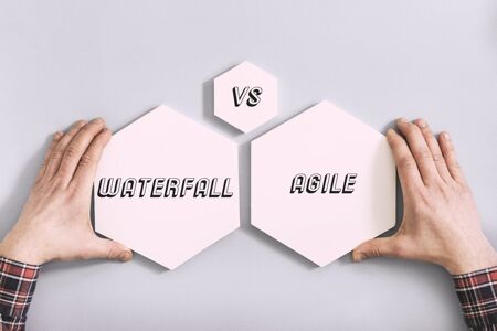 Male hands holding two pink hexagonal signs; one saying waterfall and the other saying versus agile