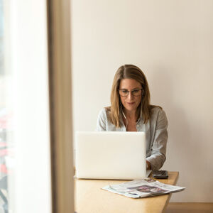 A woman is wearing a striped shirt working from home on a white laptop shot through an open door
