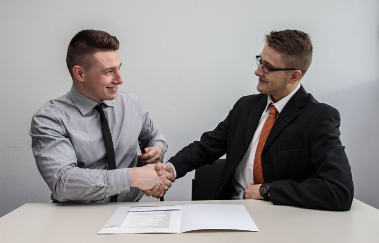 Two businessmen shaking hands in front of a document on the desk in front of them