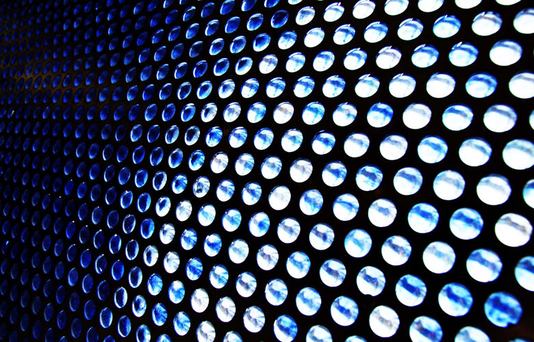 A blue metal sheet with light shining through multiple holes