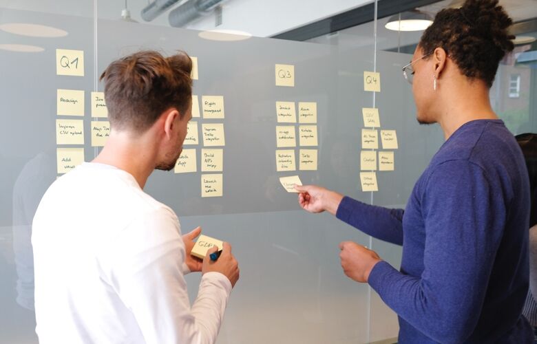 Two business people placing yellow sticky notes on a glass partition
