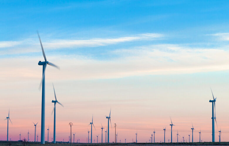 Many wind turbines in a field against a pink and blue sky